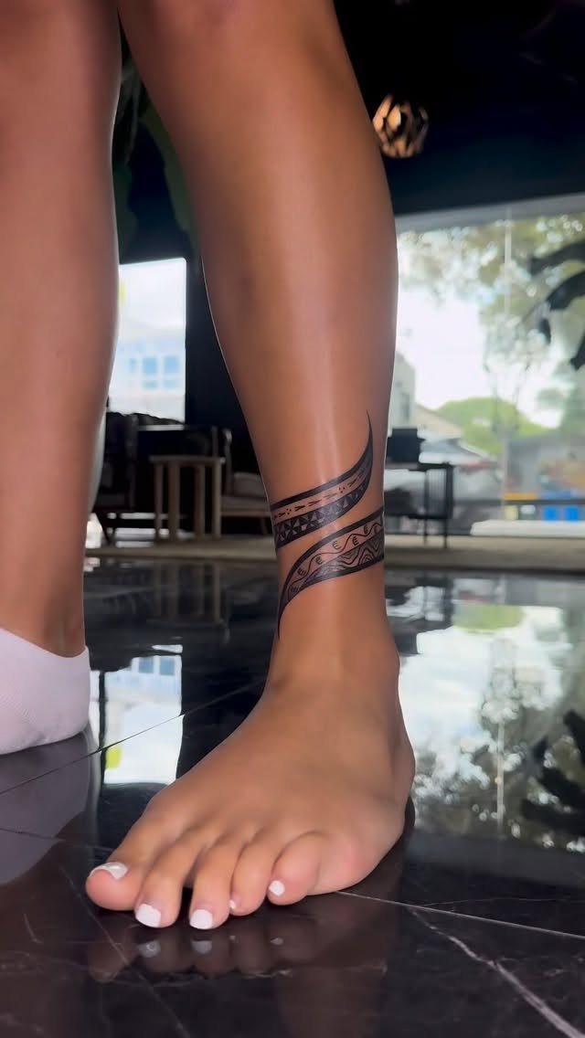 Ankle with a black ink swirling patterned band tattoo on a reflective floor
