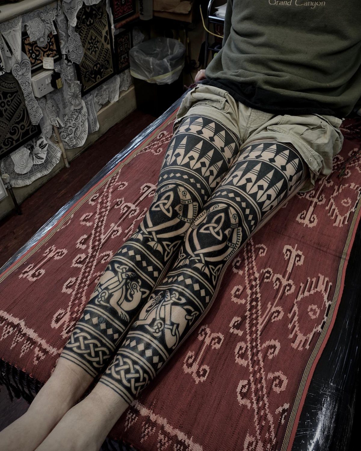 Legs with intricate black ink Celtic knot and geometric band tattoos on a rug
