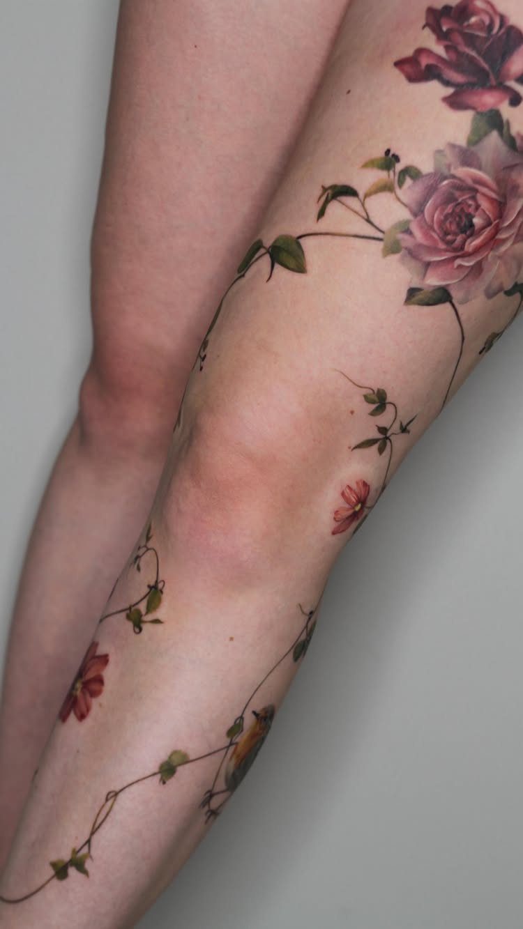 Floral leg band tattoo with pink roses and green vines wrapping around a leg.