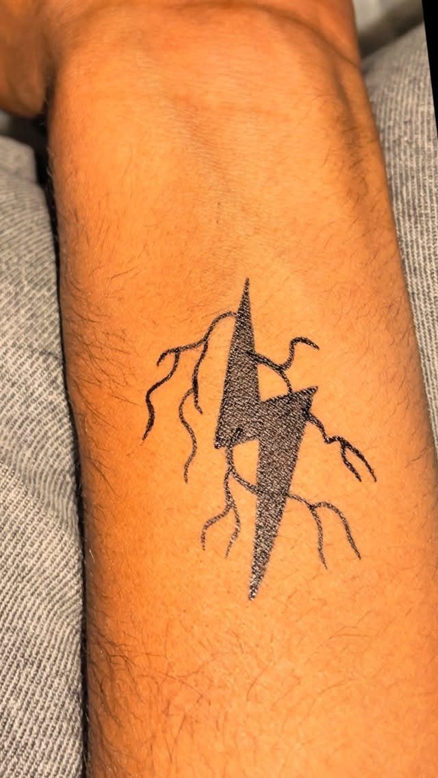 Lightning bolt tattoo with branching lines on a person's forearm.