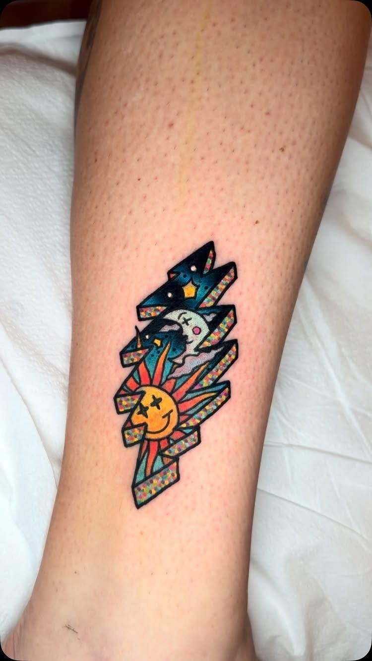 Lightning bolt tattoo on a leg featuring a smiling sun, moon, and stars.