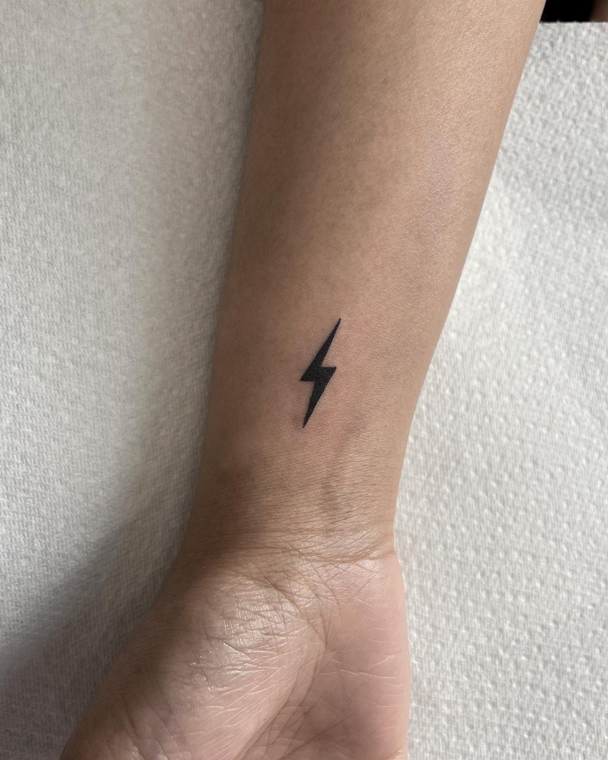 Small black lightning bolt tattoo centered on the inner wrist of an arm.