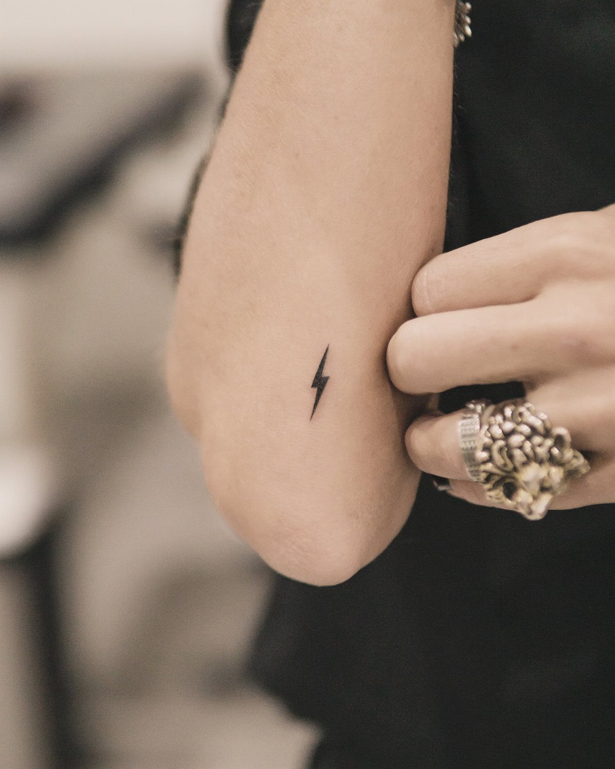 Small black lightning bolt tattoo on a person's inner wrist with silver ring
