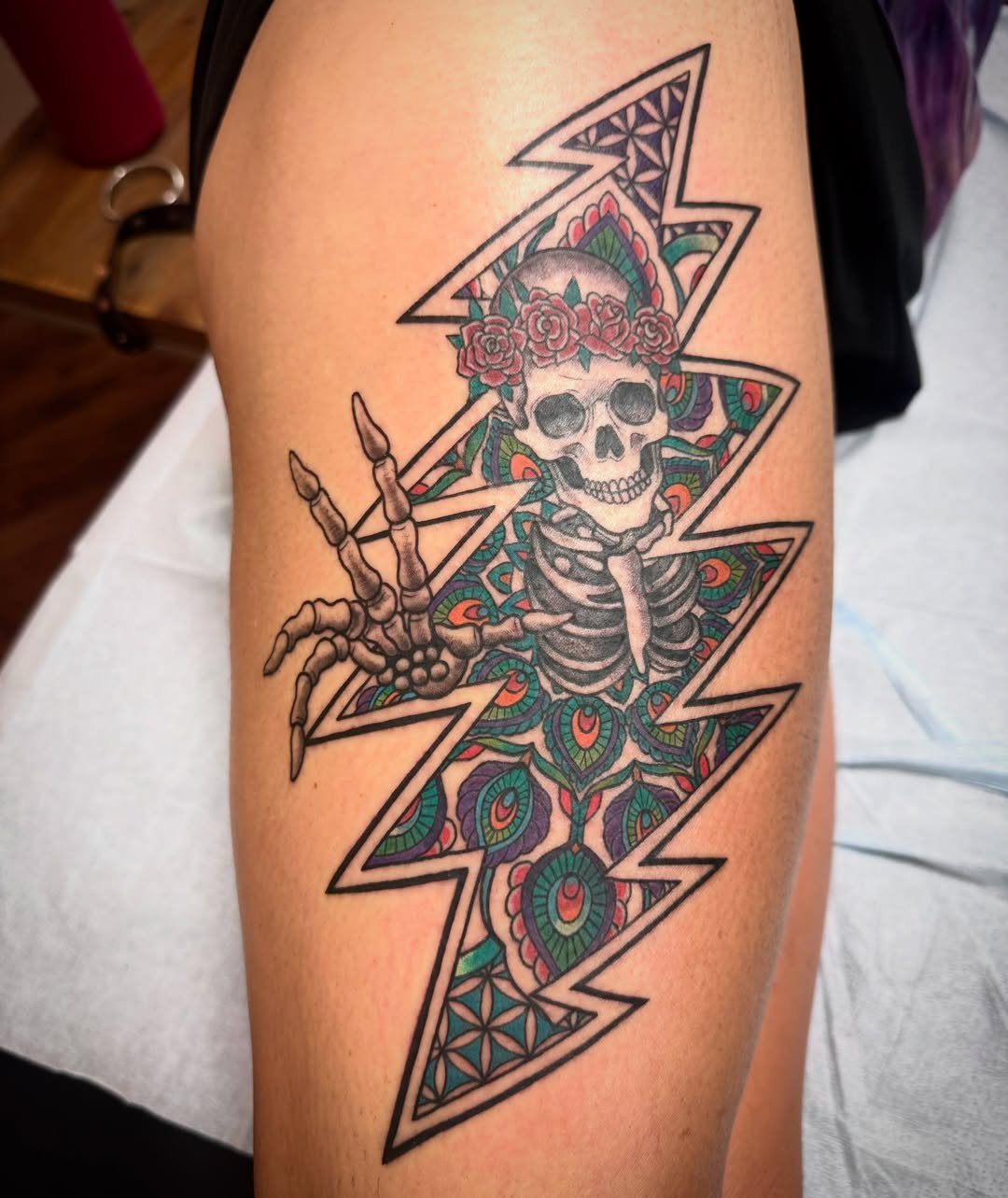 Lightning bolt tattoo containing a skull with roses and colorful mandala patterns.