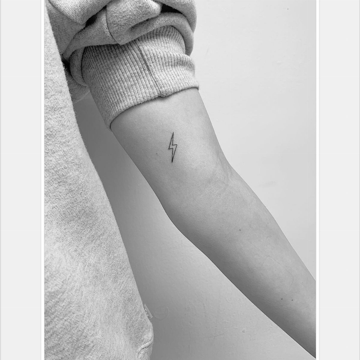 Small black lightning bolt tattoo on the inner forearm of a person.