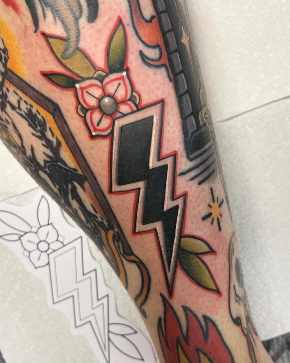 Traditional black lightning bolt tattoo with red outline and floral elements on skin.