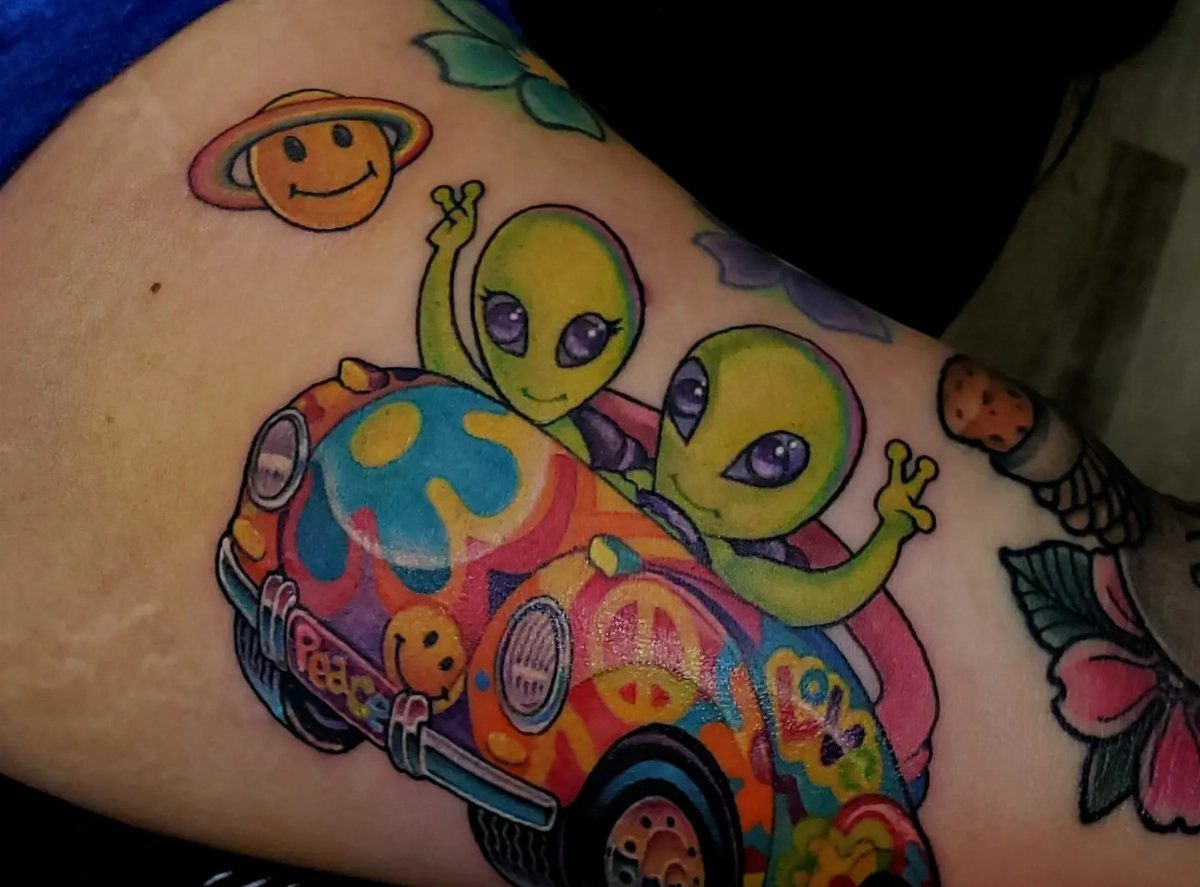 Two green aliens in a rainbow car tattoo on a person's skin