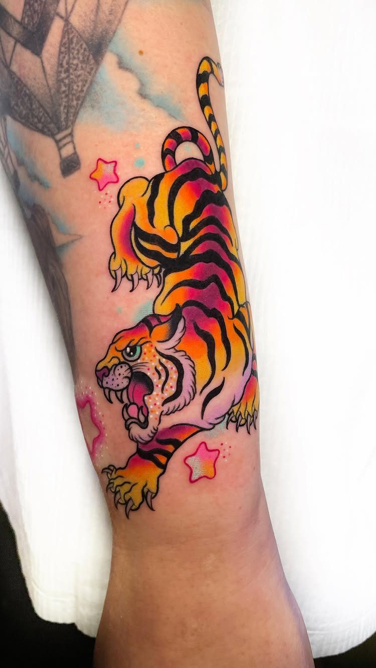 Colorful baby tiger tattoo with pink stars on a person's forearm.