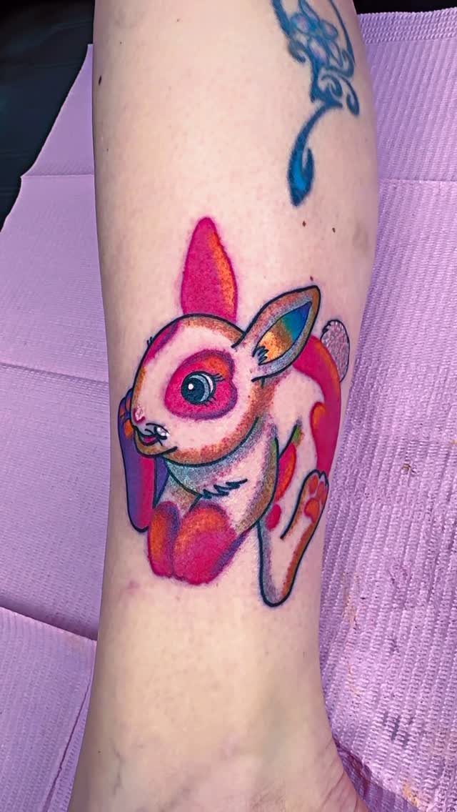 Colorful stylized bunny tattoo with pink and purple hues on a person's ankle.