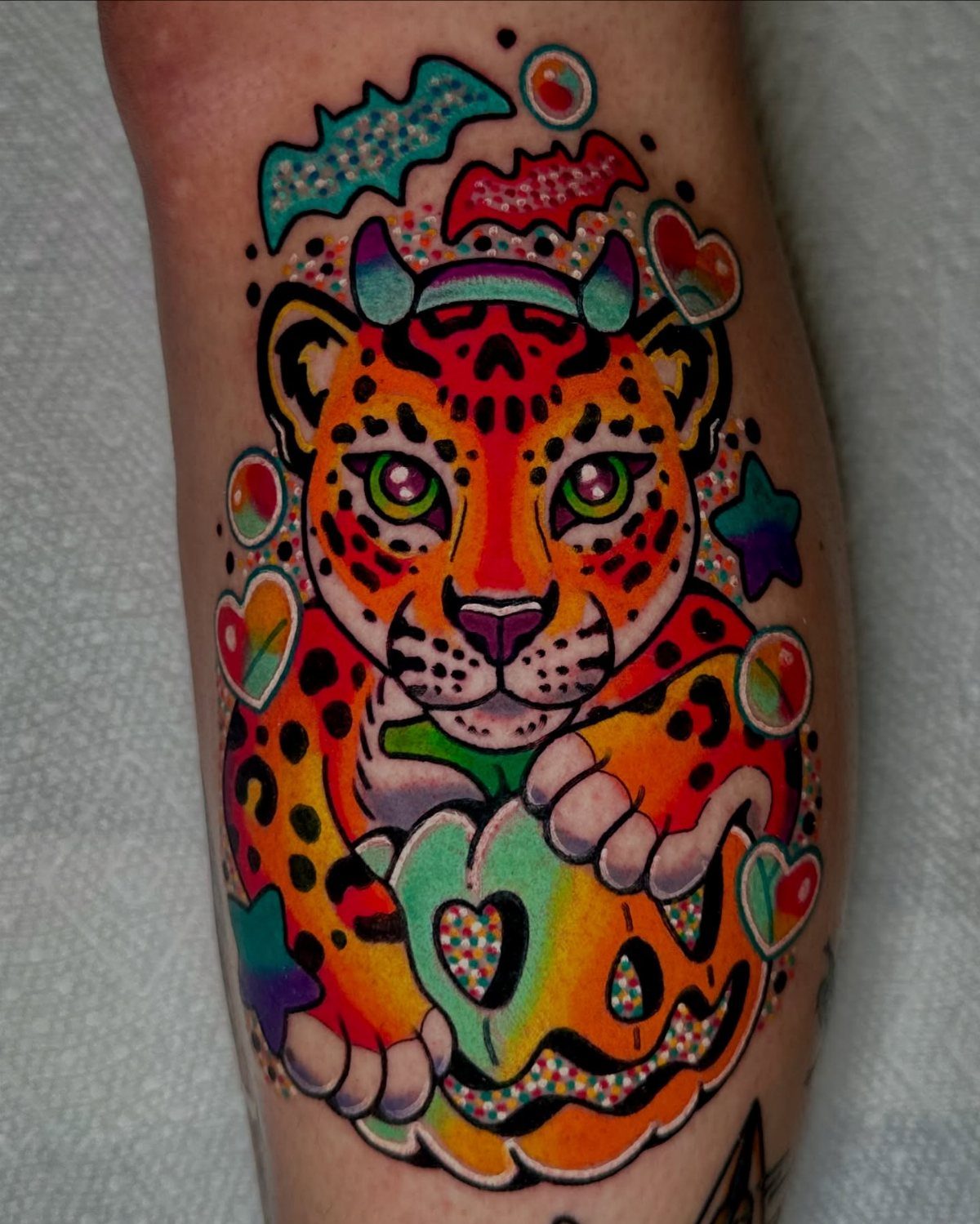 Rainbow leopard tattoo holding a colorful pumpkin with stars and hearts on skin