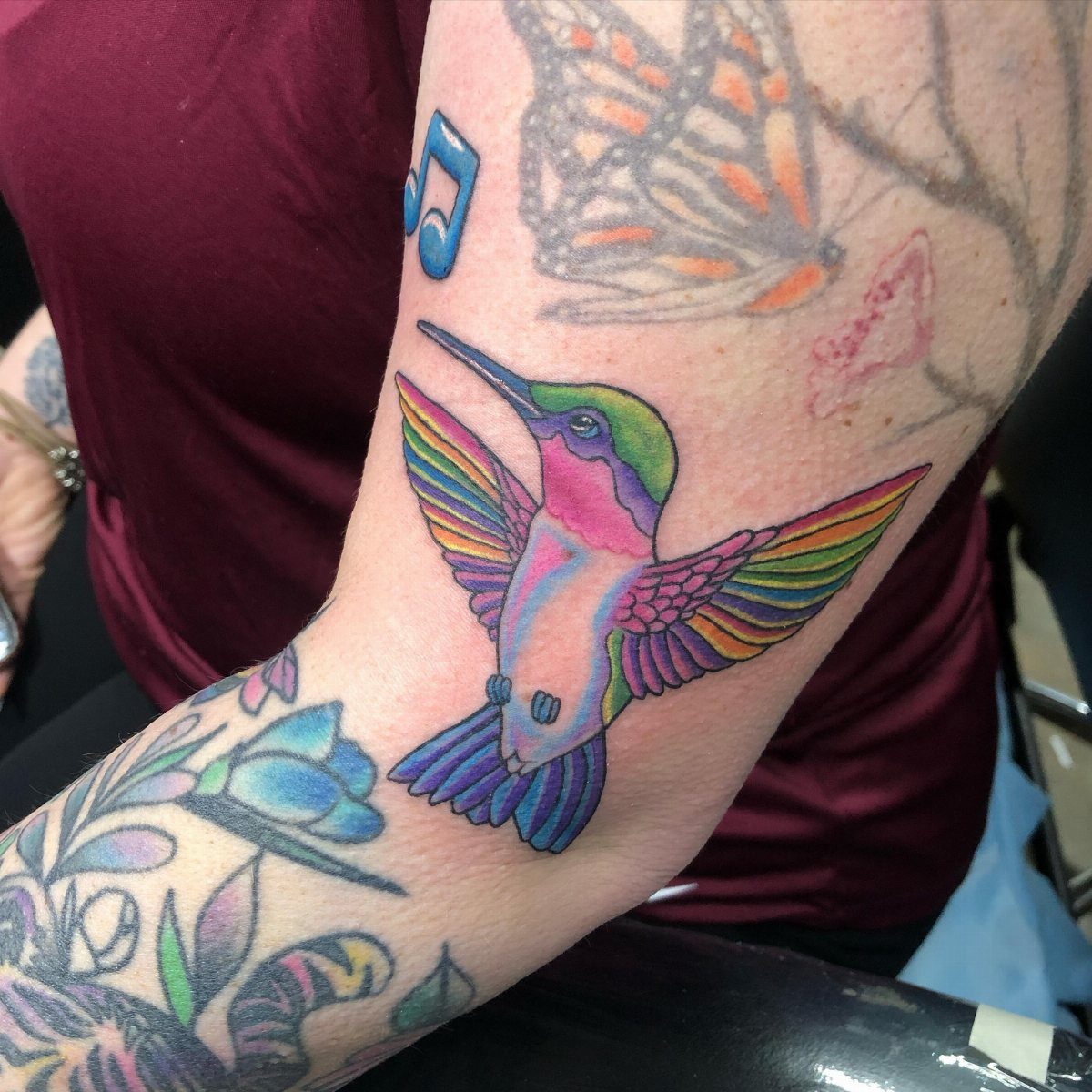 Rainbow hummingbird tattoo with vibrant gradient colors on a person's forearm.