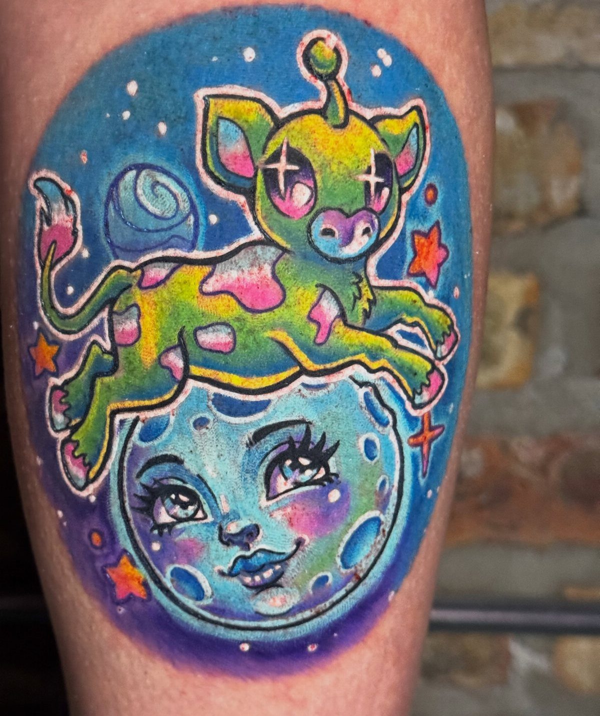Colorful tattoo of a neon green cow and a blue moon face on skin.