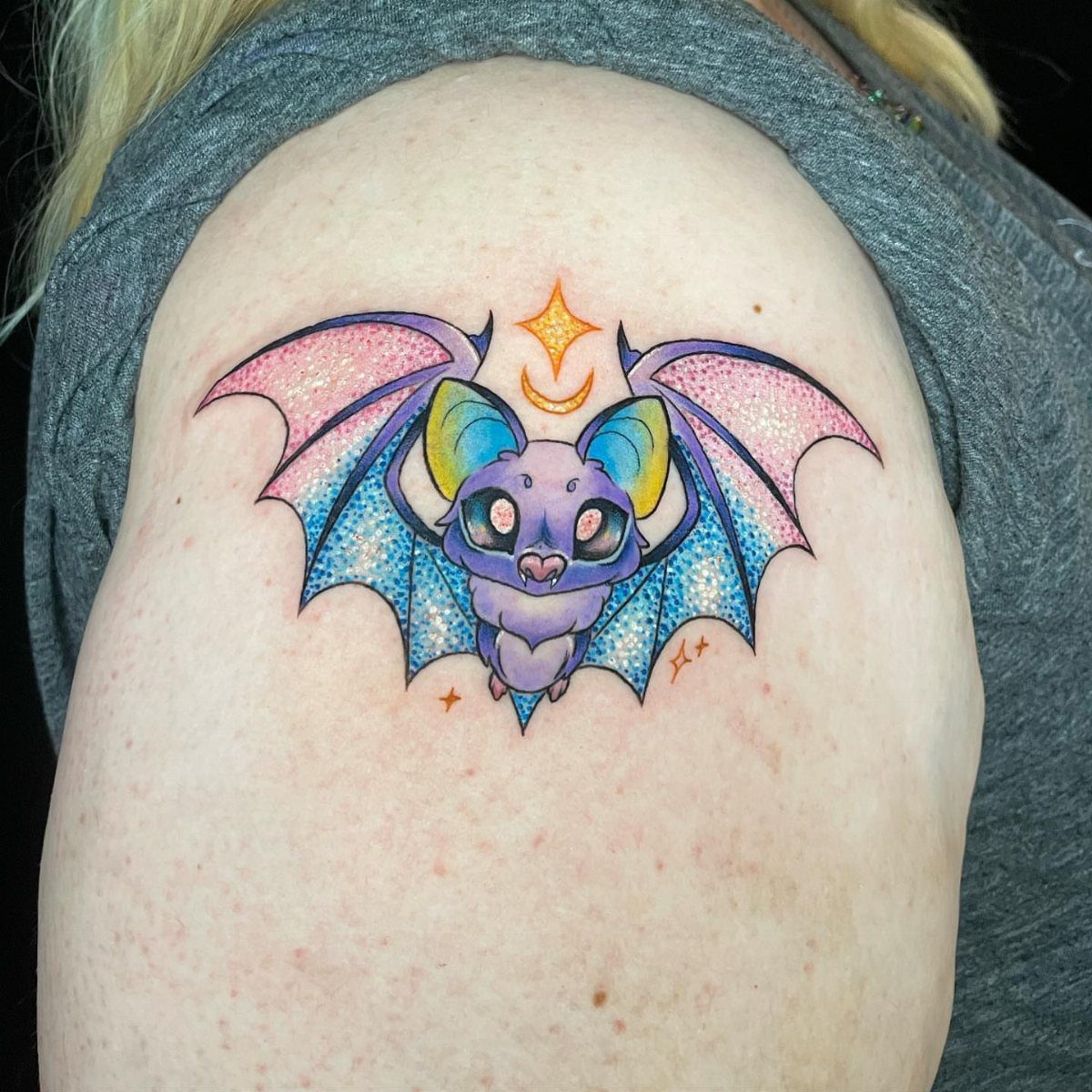 Colorful rainbow bat tattoo with sparkling wings on a person's shoulder