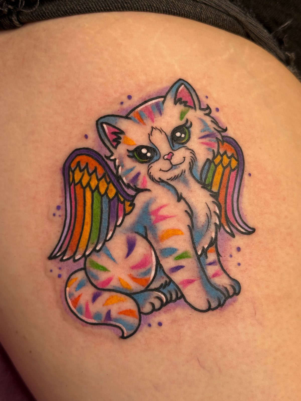 Rainbow winged kitten tattoo with colorful stripes on a person's skin.