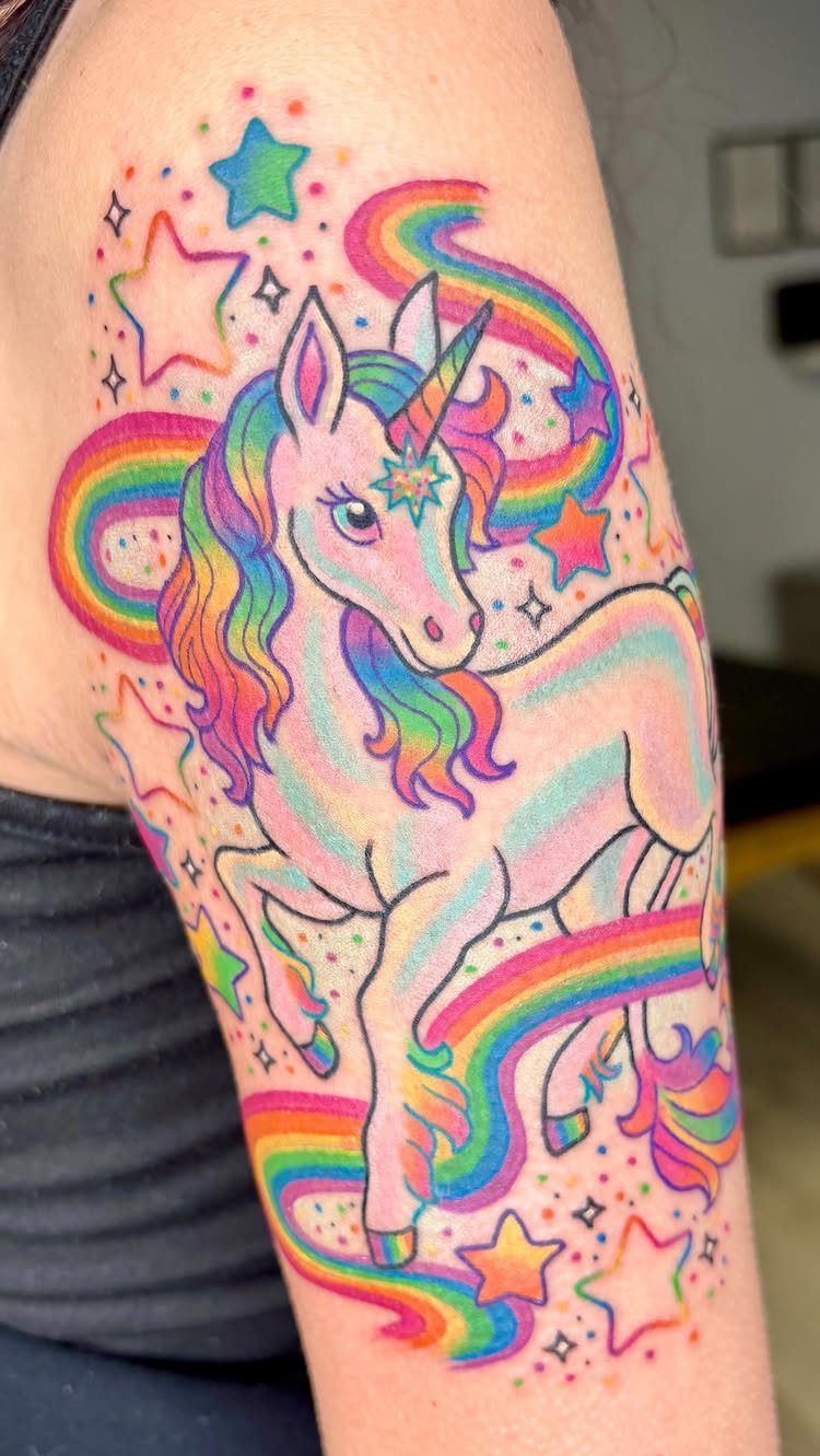 Rainbow unicorn tattoo with colorful stars and swirls on a person's arm.