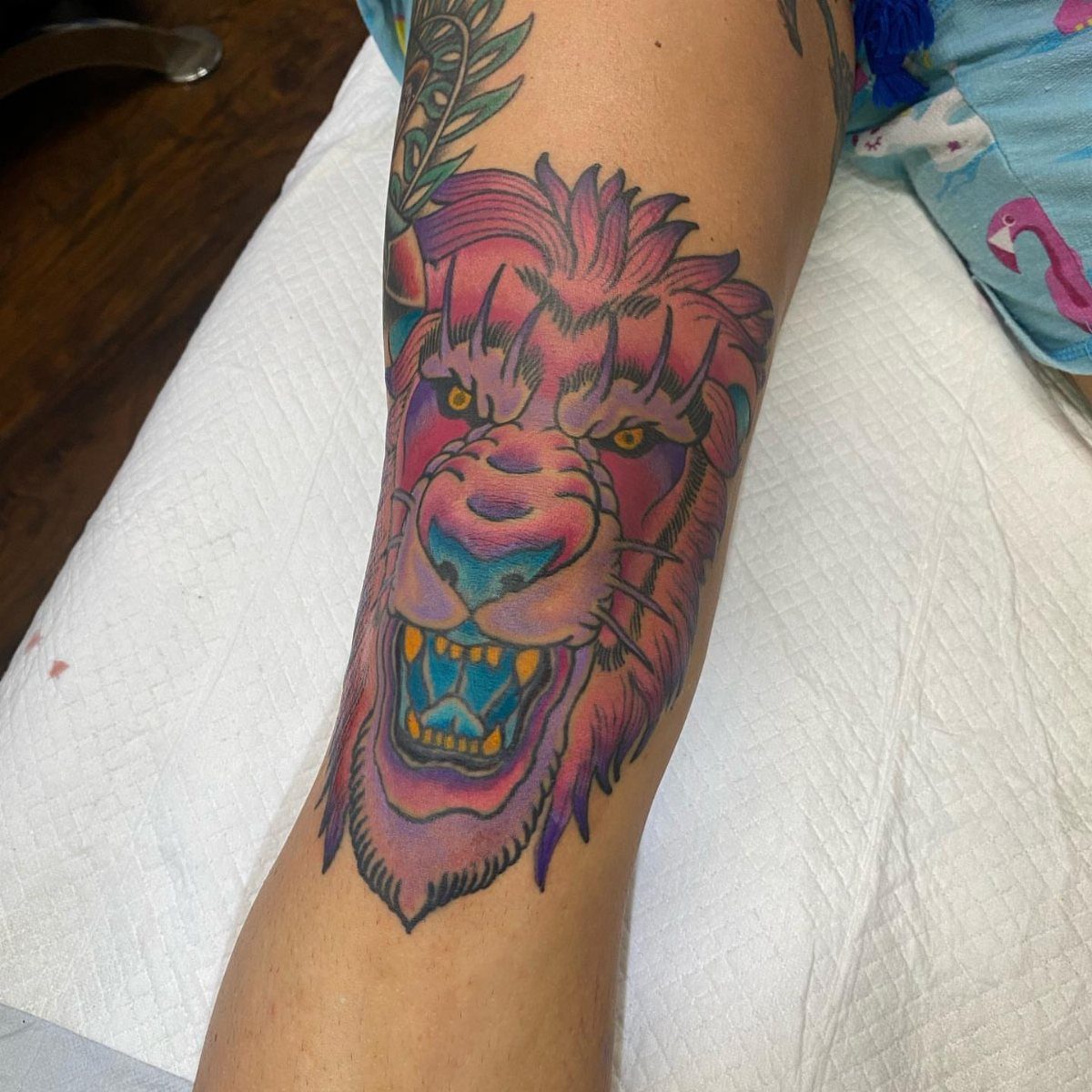 Colorful roaring lion tattoo with pink and purple hues on a person's leg.
