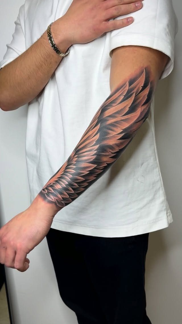 Detailed black and grey wing tattoo on a man's forearm wearing a white shirt.