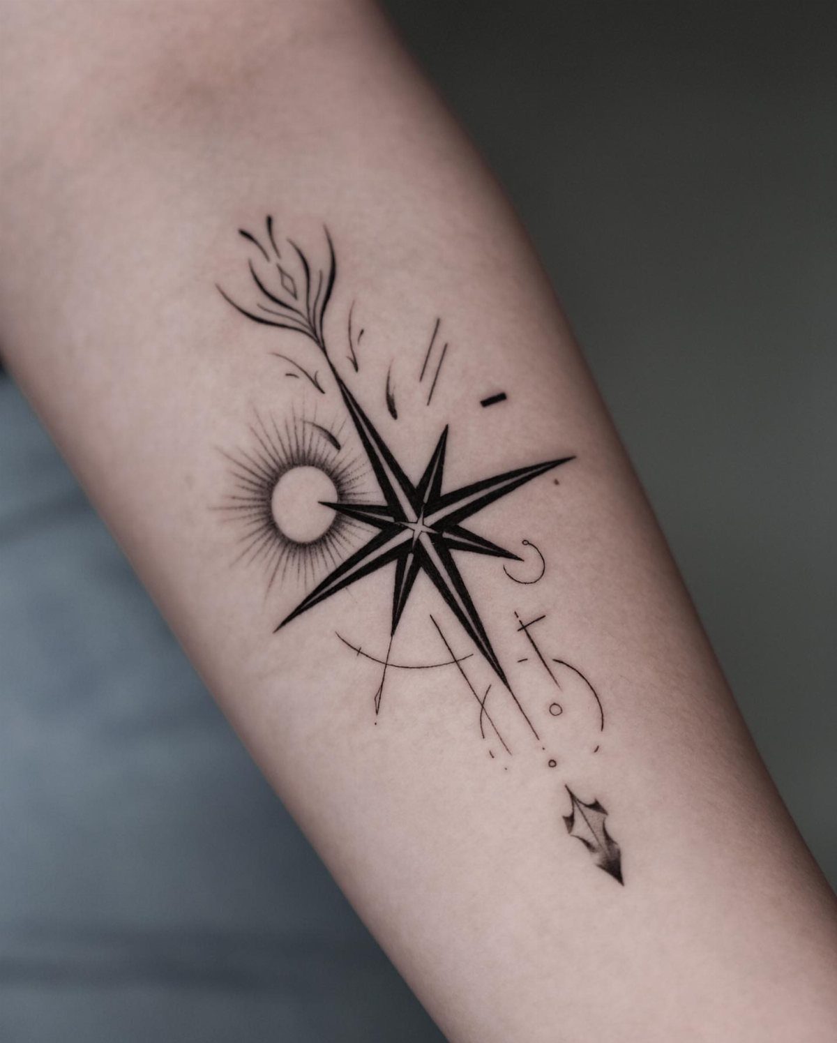 Black ink tattoo of an arrow and star on a person's forearm.