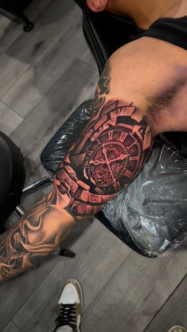 Detailed clock tattoo with Roman numerals and red accents on a man's arm.