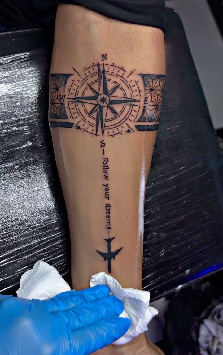 Compass rose tattoo on a lower leg with a plane and inspirational quote.