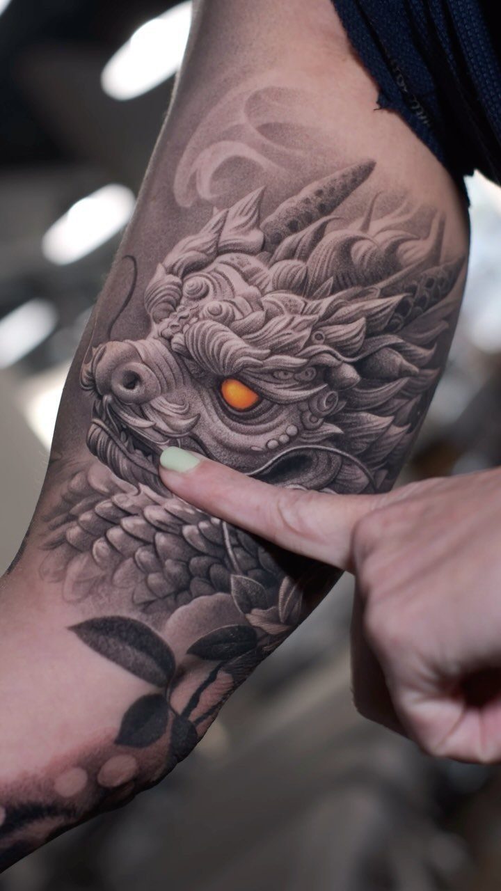 Detailed black and grey dragon tattoo on an arm with a glowing orange eye.