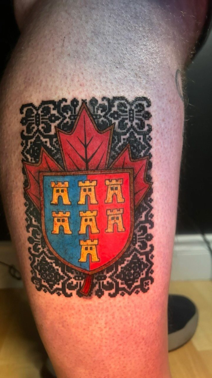 Family crest tattoo on a leg featuring a maple leaf and shield.