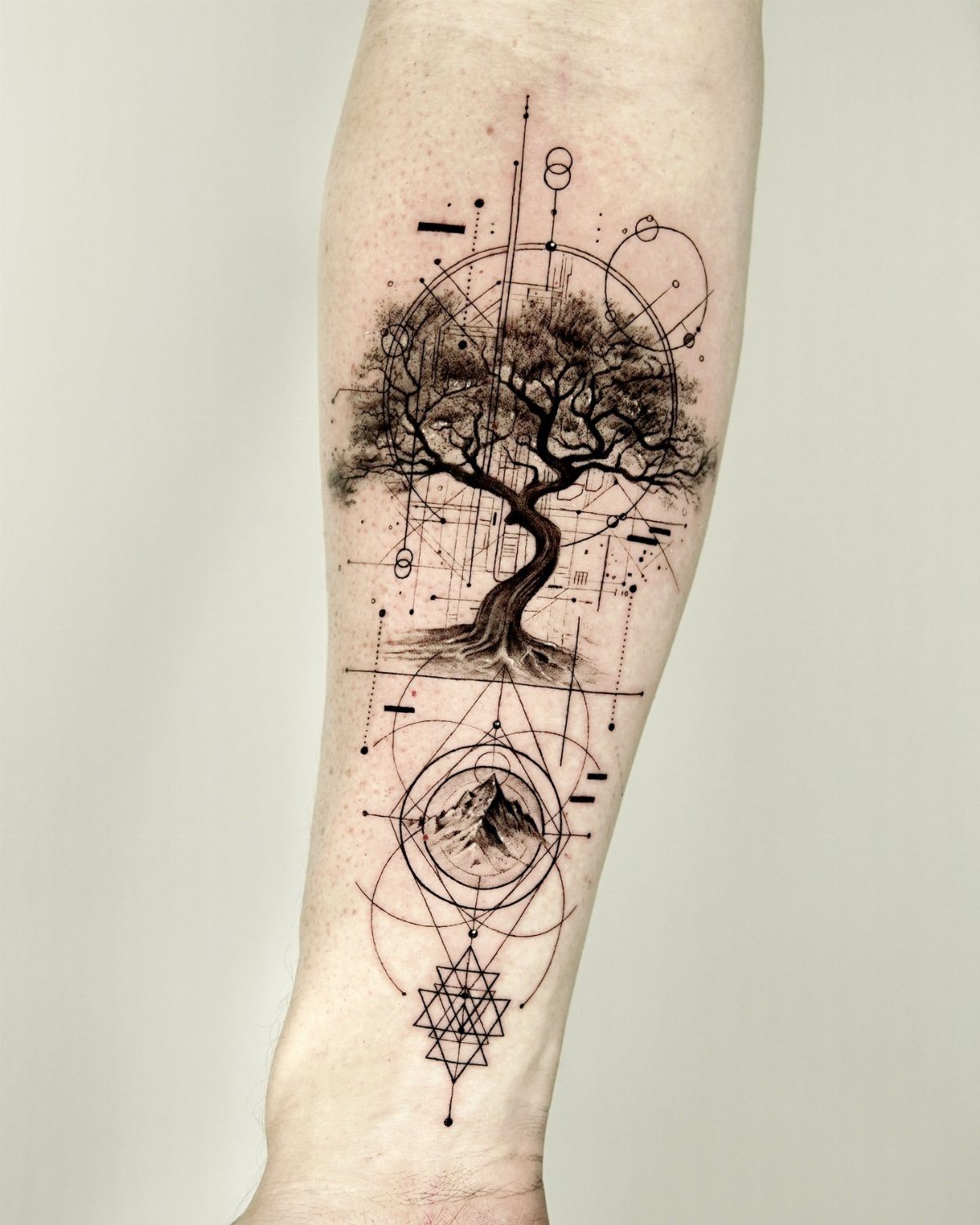 Tree tattoo on a forearm with geometric shapes and a mountain peak.