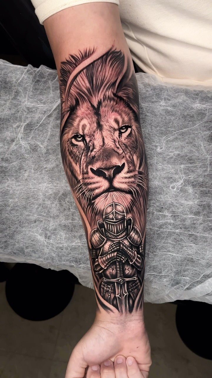Lion and kneeling knight tattoo in black and grey ink on a man's forearm