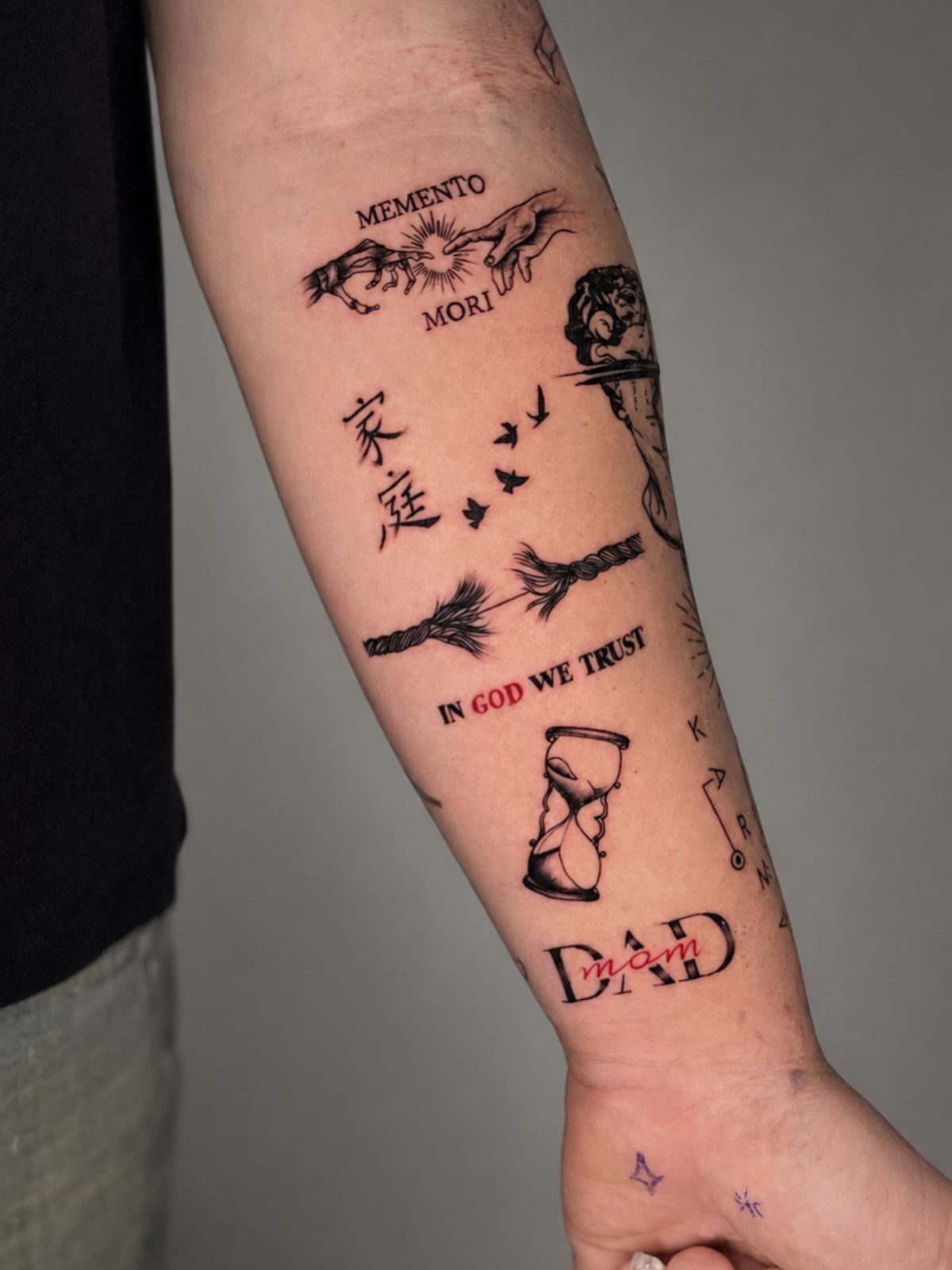 Man's forearm with multiple small minimalist black ink tattoos including text and symbols.