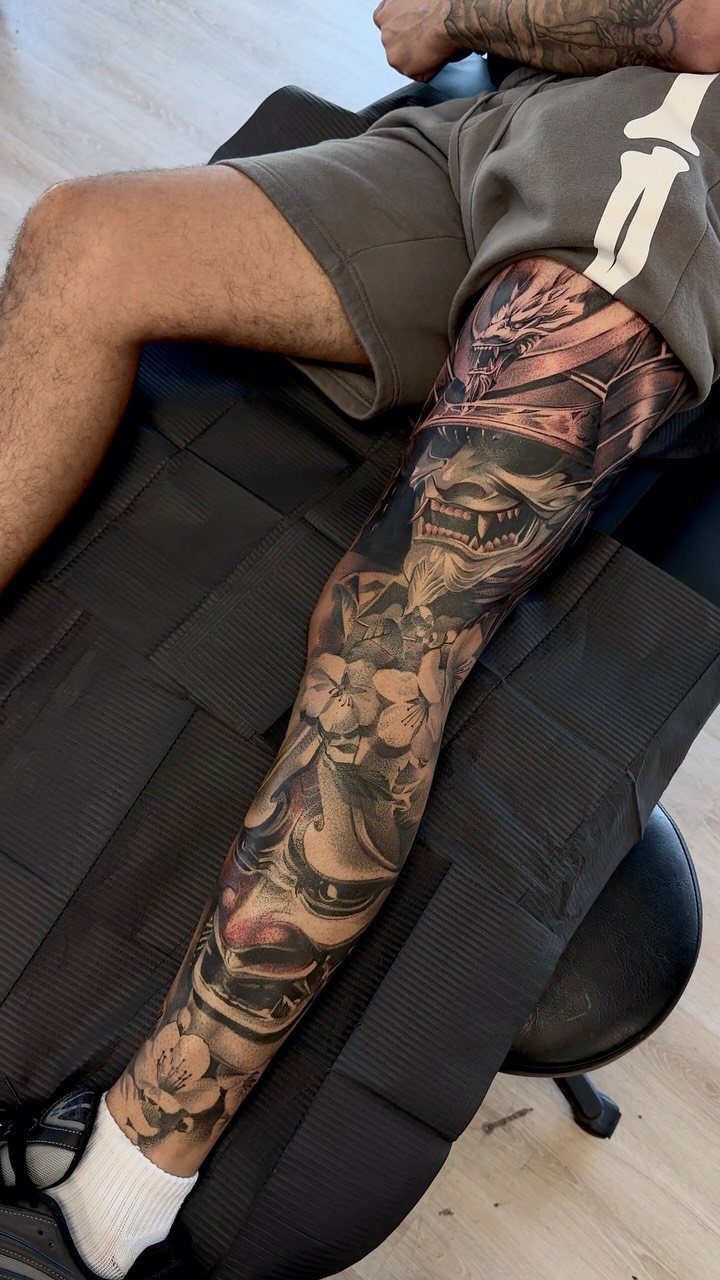 Samurai mask and demonic figure tattoo on a man's lower leg with cherry blossoms