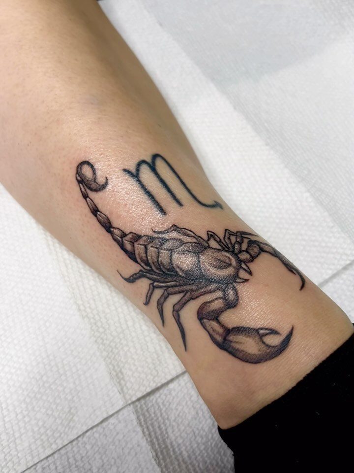 Scorpio zodiac tattoo on a forearm featuring a realistic scorpion and astrological symbol.