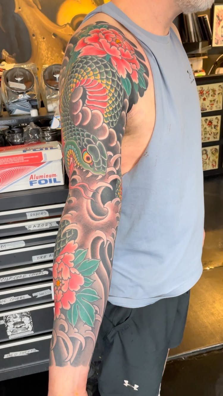 Snake tattoo sleeve with red peonies and grey clouds on a man's arm