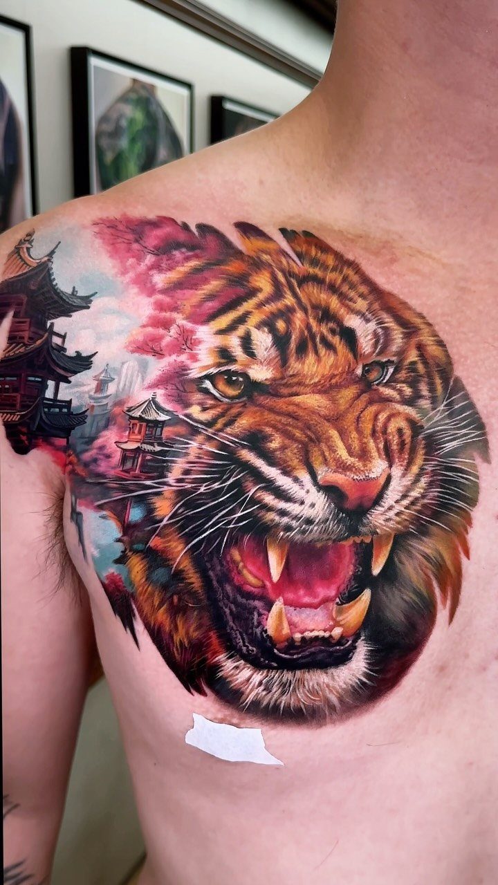 Roaring tiger tattoo on a man's chest with traditional Asian buildings and clouds.