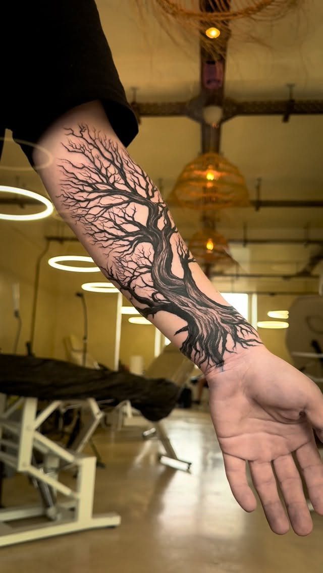 Detailed black ink tree tattoo with bare branches on a man's forearm.