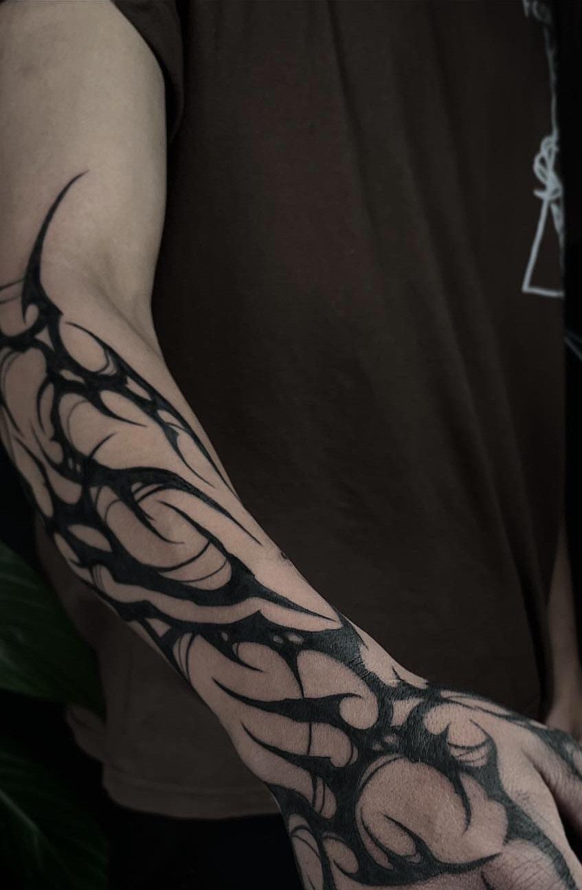 Bold black tribal tattoo with flowing curved lines on a man's forearm and hand.