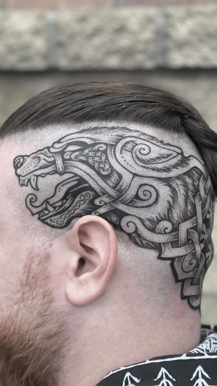 Stylized wolf head tattoo with Celtic knotwork on a man's side scalp