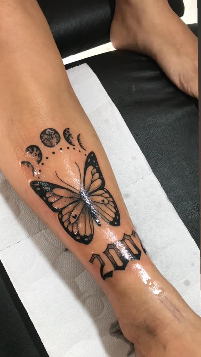 Butterfly and moon phase tattoo on a lower leg with the year 2001.