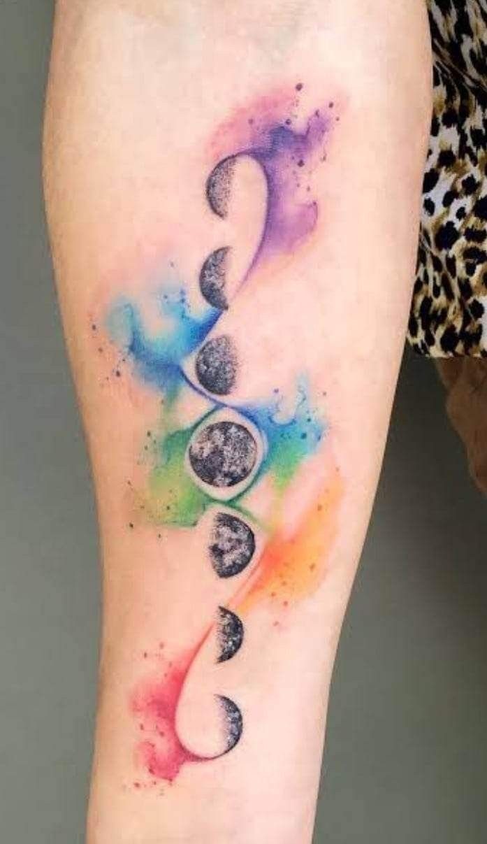 Moon phase tattoo on an arm with colorful watercolor chakra splashes.