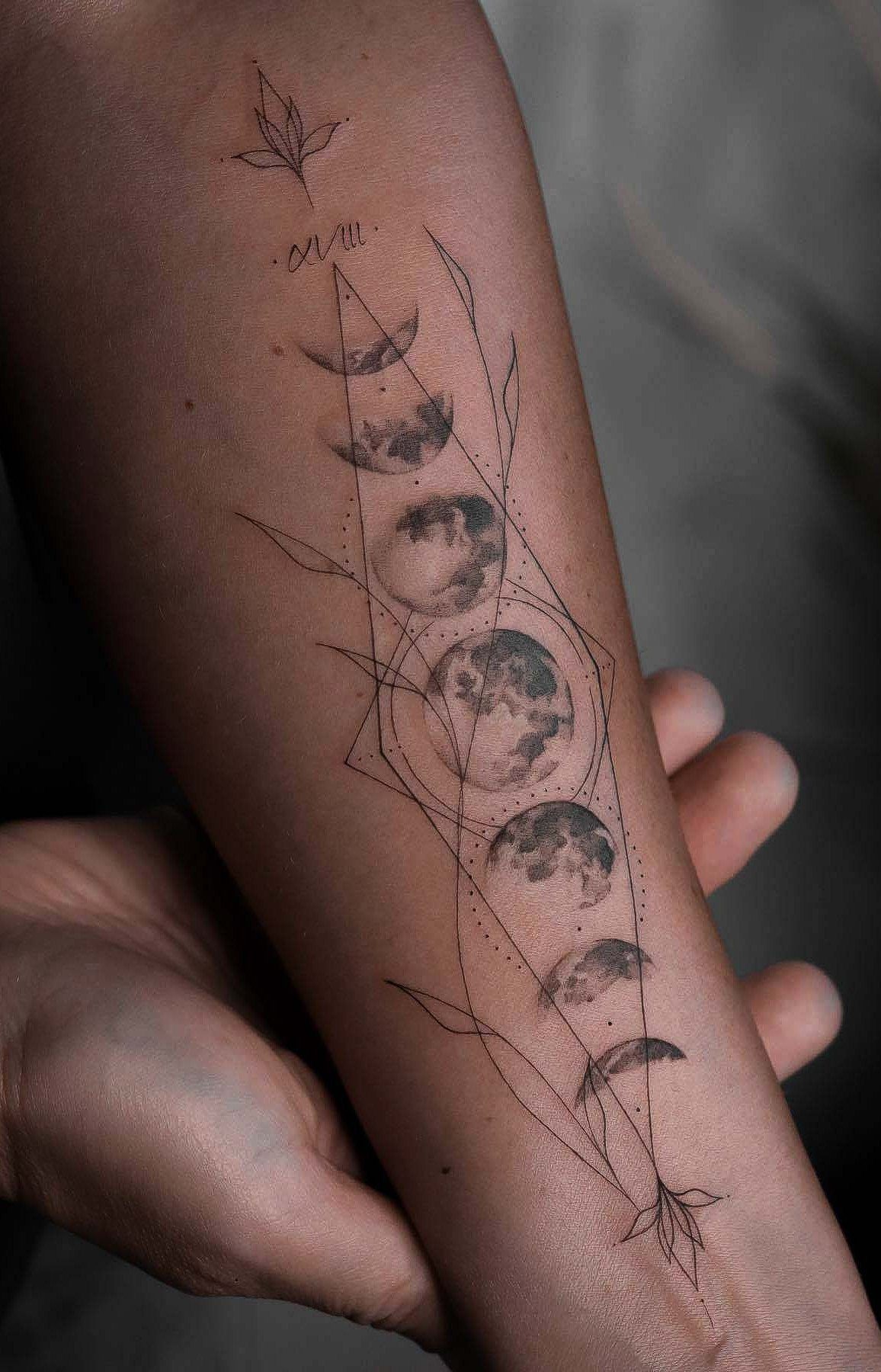 Moon phase tattoo on a forearm enclosed in a geometric diamond frame with leaves.