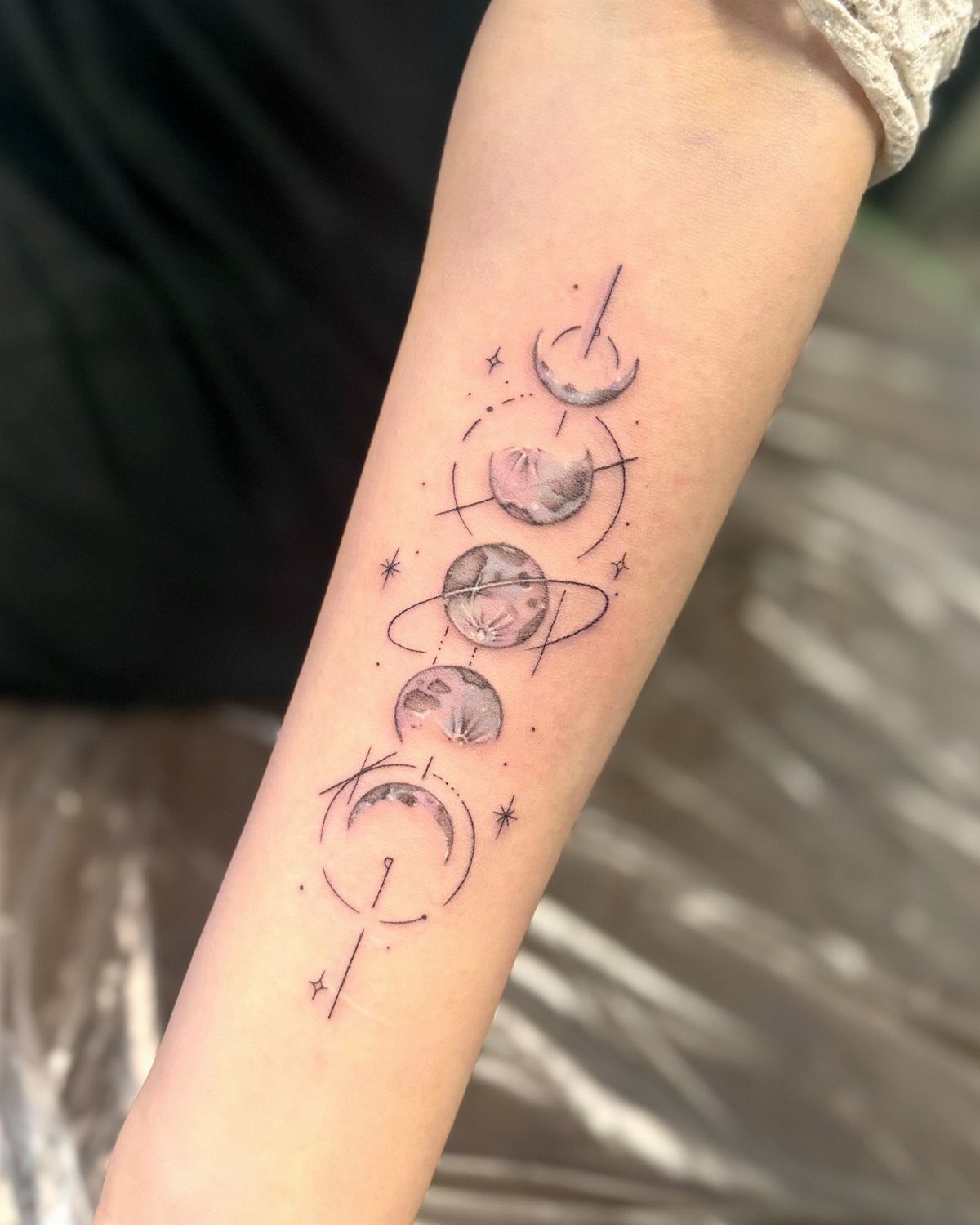 Moon phase tattoo on a forearm featuring lunar cycles and small decorative stars.