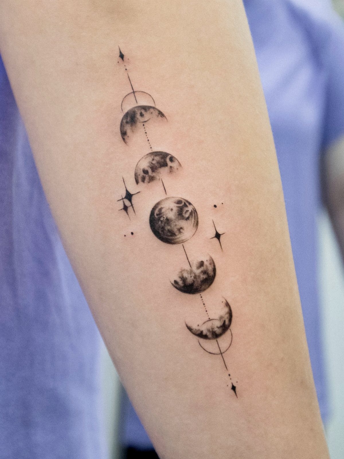 Moon cycle tattoo on an arm with detailed phases and small stars.