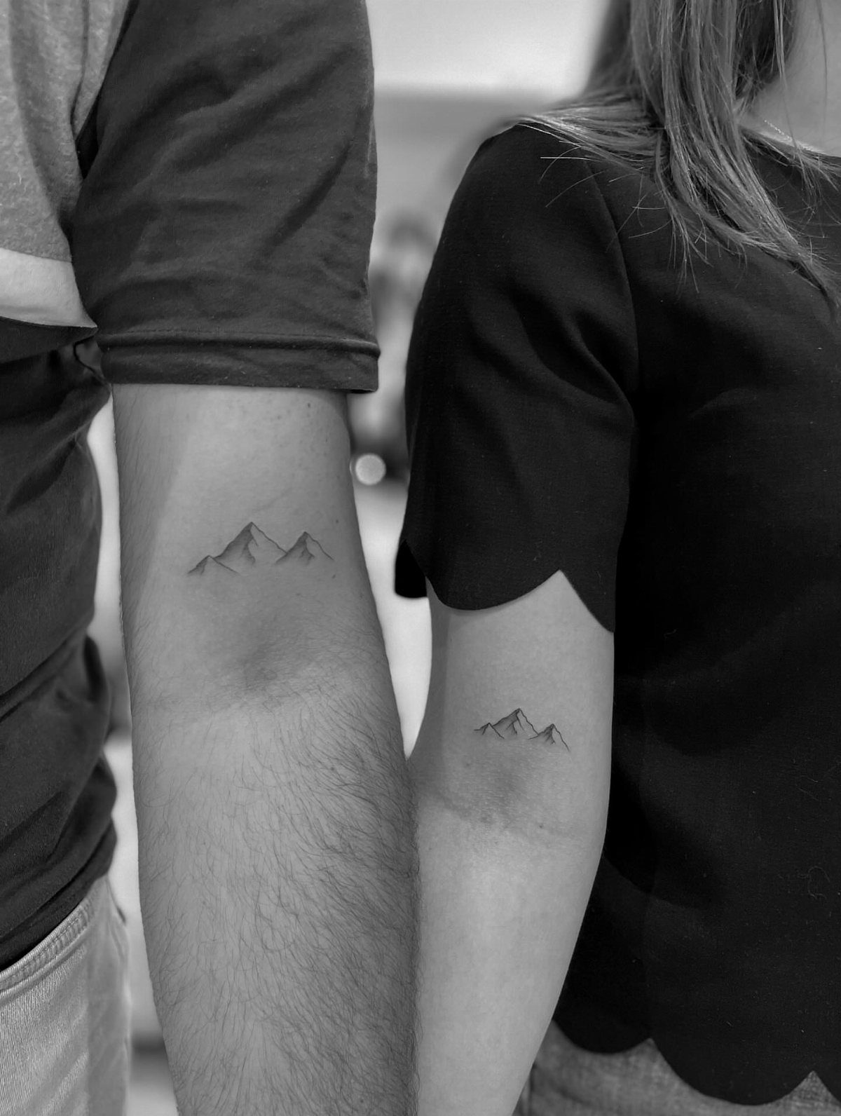 Small minimalist mountain range tattoos on the inner forearms of two people.