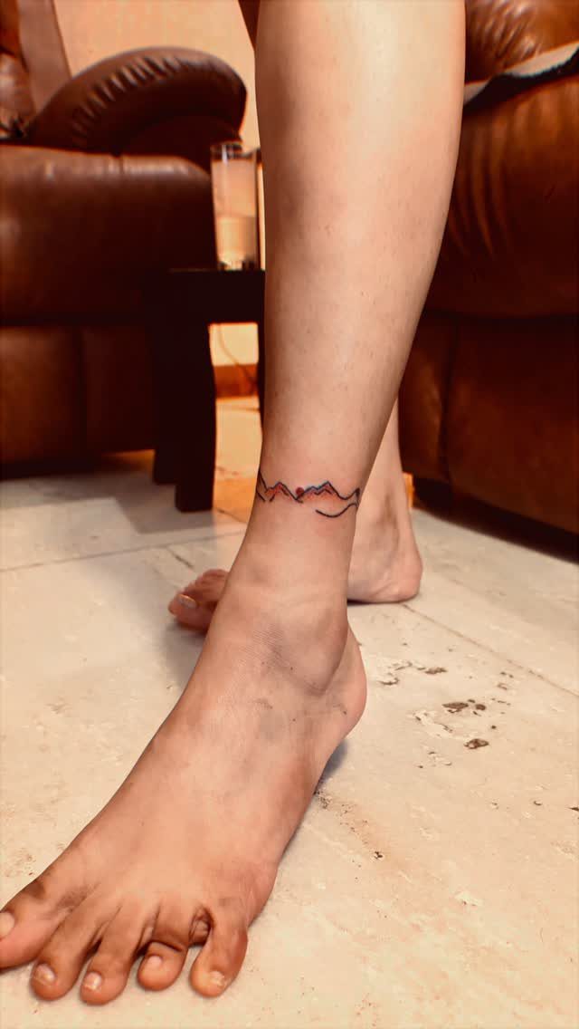 Mountain range tattoo wrapped around a person's ankle on a light floor