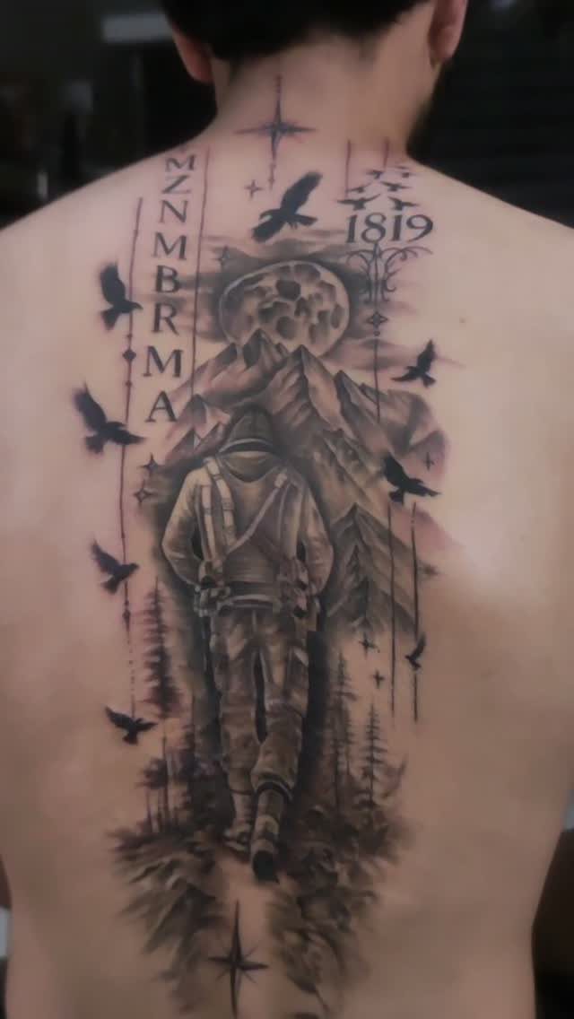Detailed black and grey back tattoo of a hooded figure and mountains.