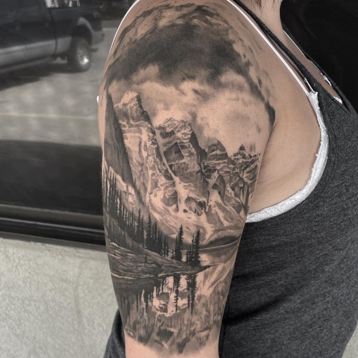 Mountain valley tattoo on an arm featuring peaks, pine trees, and a lake.