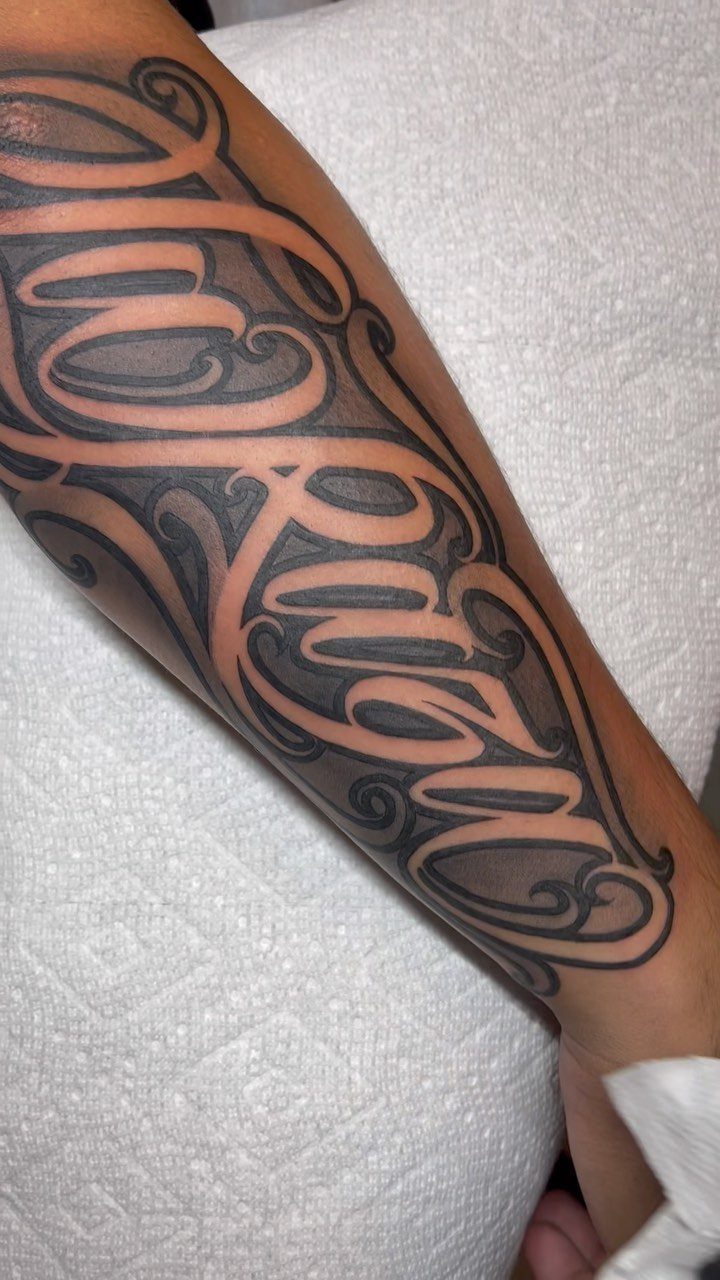 Cursive negative space lettering tattoo in black ink on a person's forearm