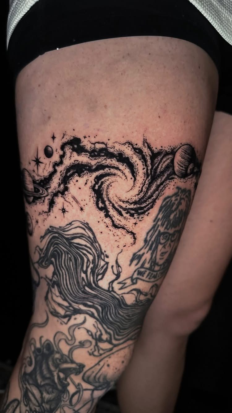 Galaxy tattoo with swirling stars and planets on a person's thigh.
