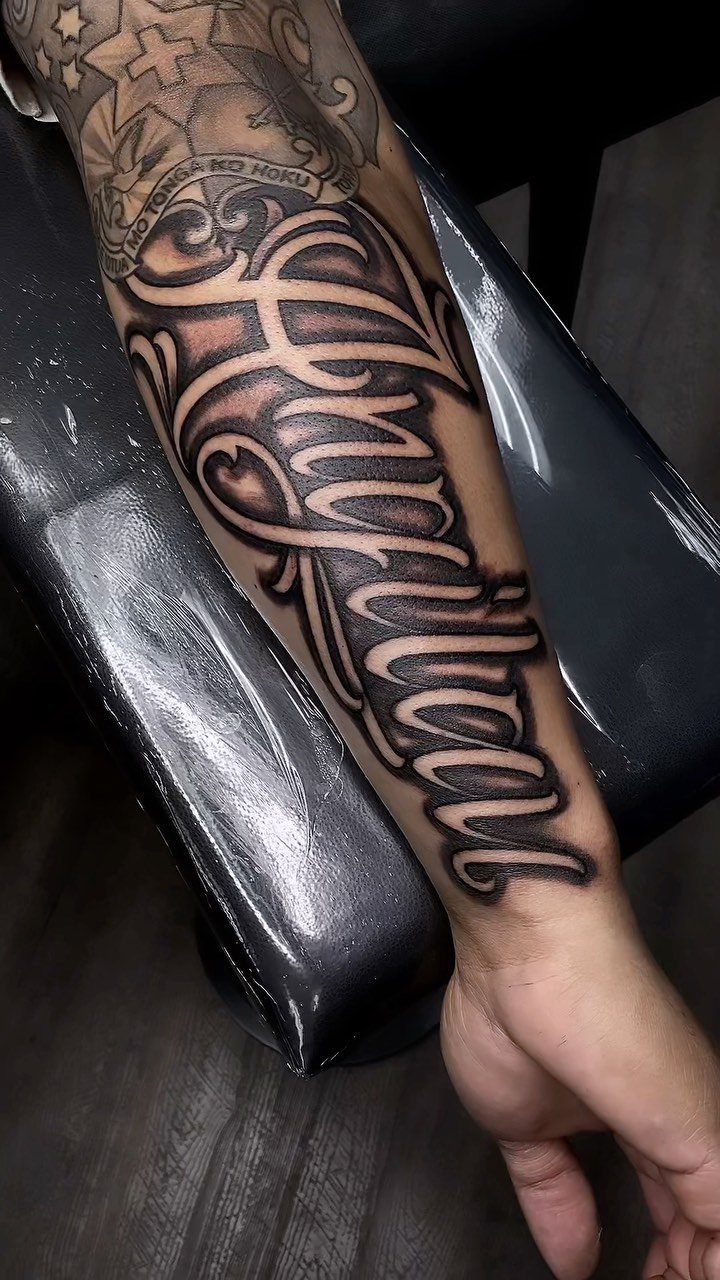Stylized negative space lettering tattoo on a person's forearm with bold black shading.