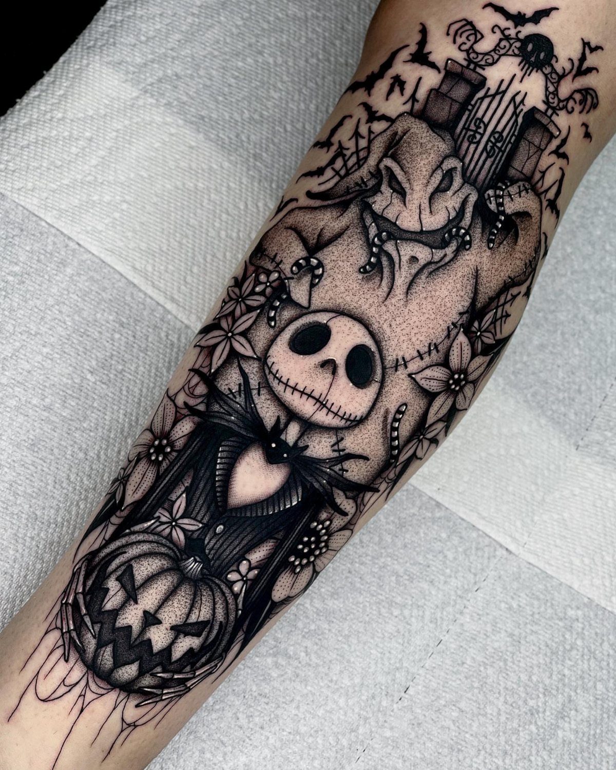 Black and grey tattoo of Jack Skellington and Oogie Boogie on a person's arm.