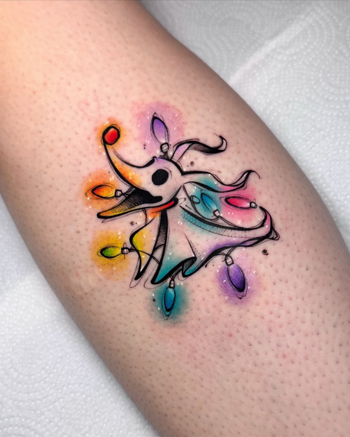 Jack Skellington tattoo wrapped in colorful Christmas lights with watercolor splashes on skin.